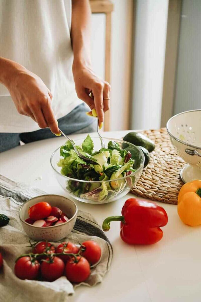 Donna che condisce insalata in ciotola di vetro  con peperoni e pomodorini vicino