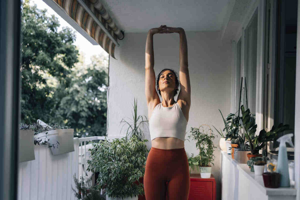 Donna che fa stretching con braccia in alto in cortile