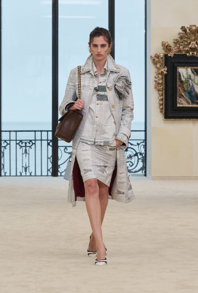 Modella con look newspaper print alla sfilata Chanel Resort