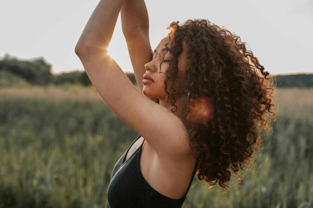 Ragazza con occhi socchiusi e mani in alto in campo verde con capelli ricci