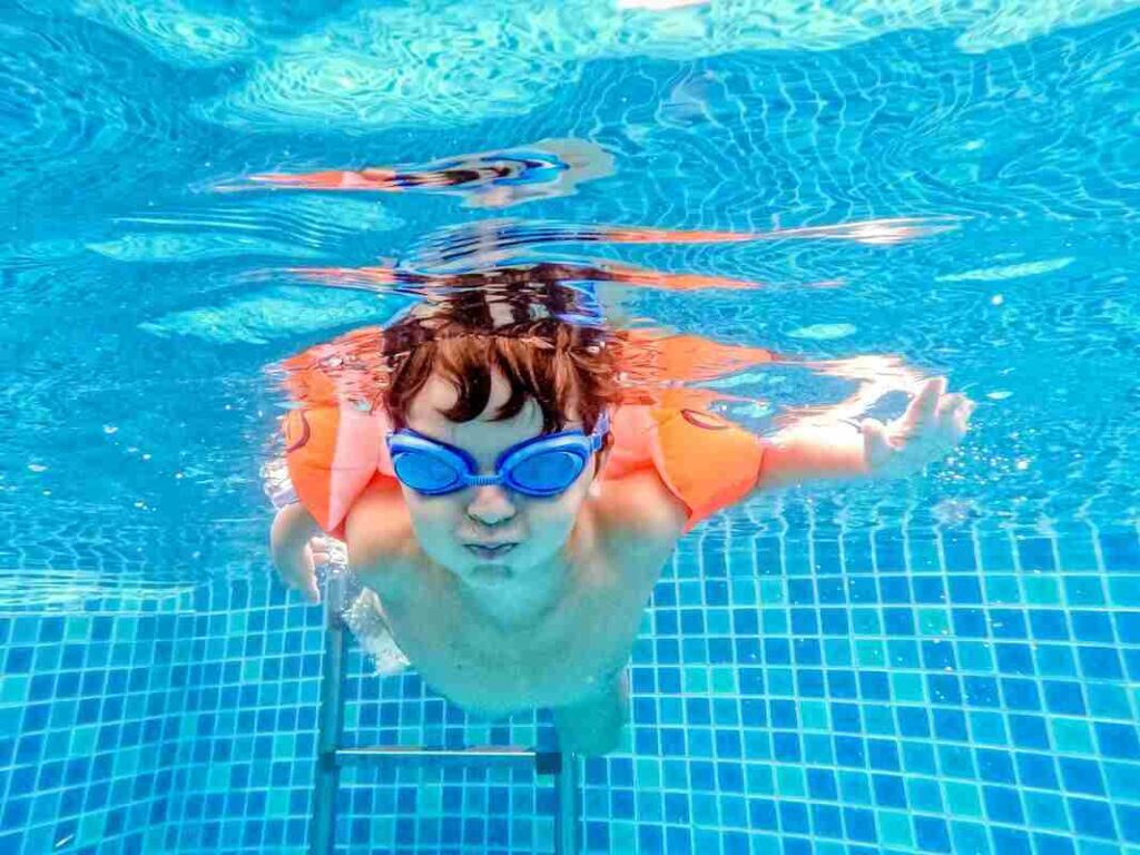 Bambino in piscina sotto l'acqua con occhialini e braccioli