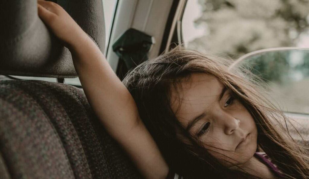Bambina in macchina con braccio alzato e sguardo triste