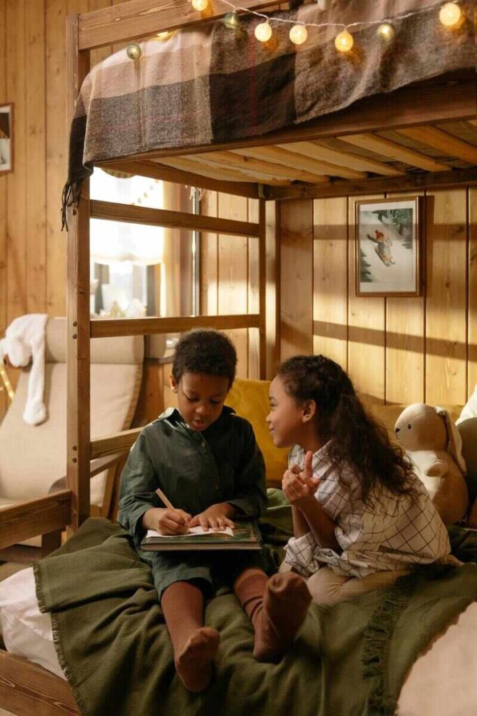 Due bambini in cameretta su letto a castello con libro in mano