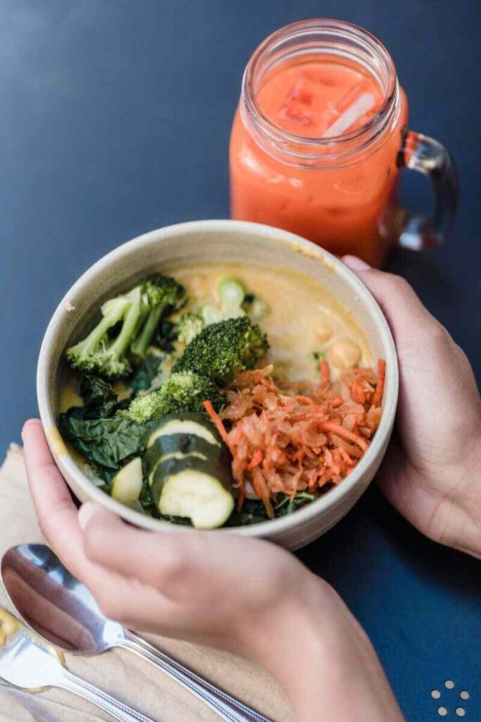ciotola con zucchine, carote e broccoli tra mani e bicchiere con succo