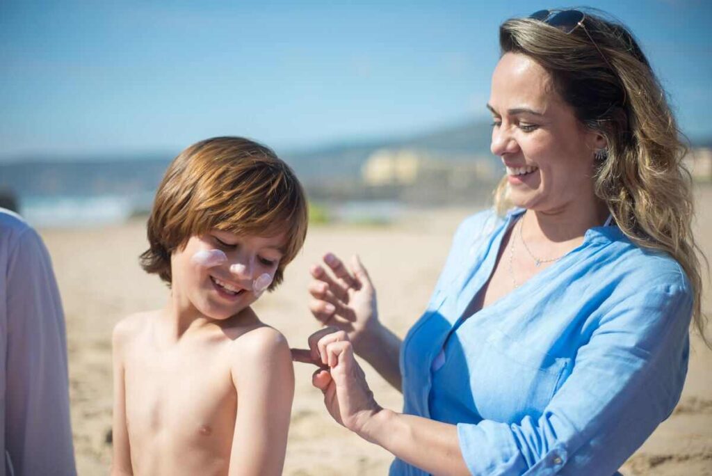 Mama che mette crema solare al bambino in spiaggia