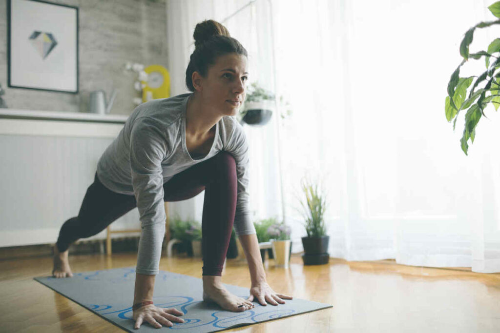 Donna su tappetino con gamba in avanti e sguardo in avanti che fa yoga