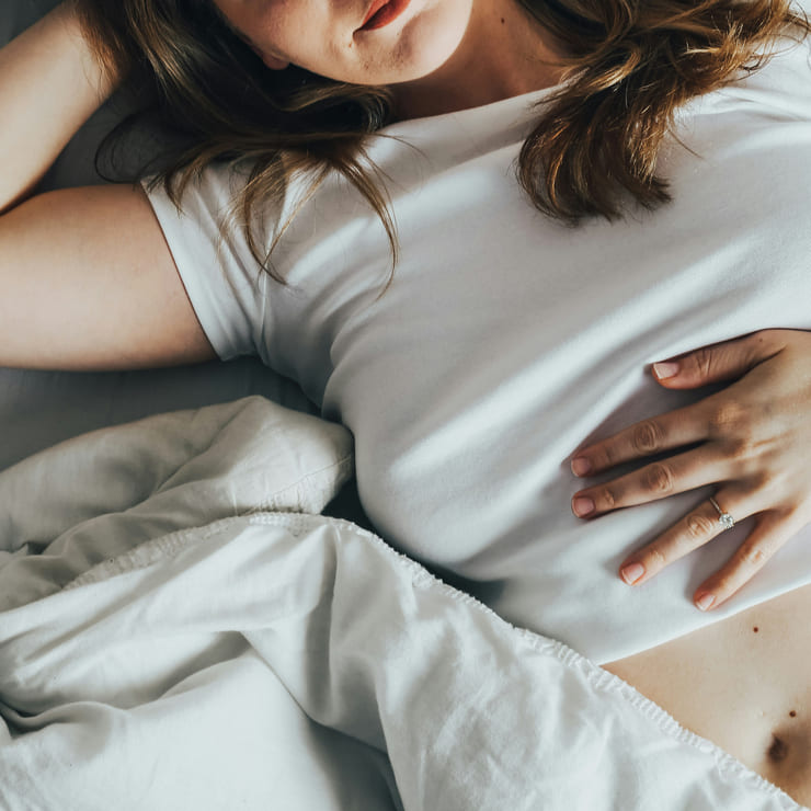 Un donna stesa a letto si tiene una mano sulla pancia