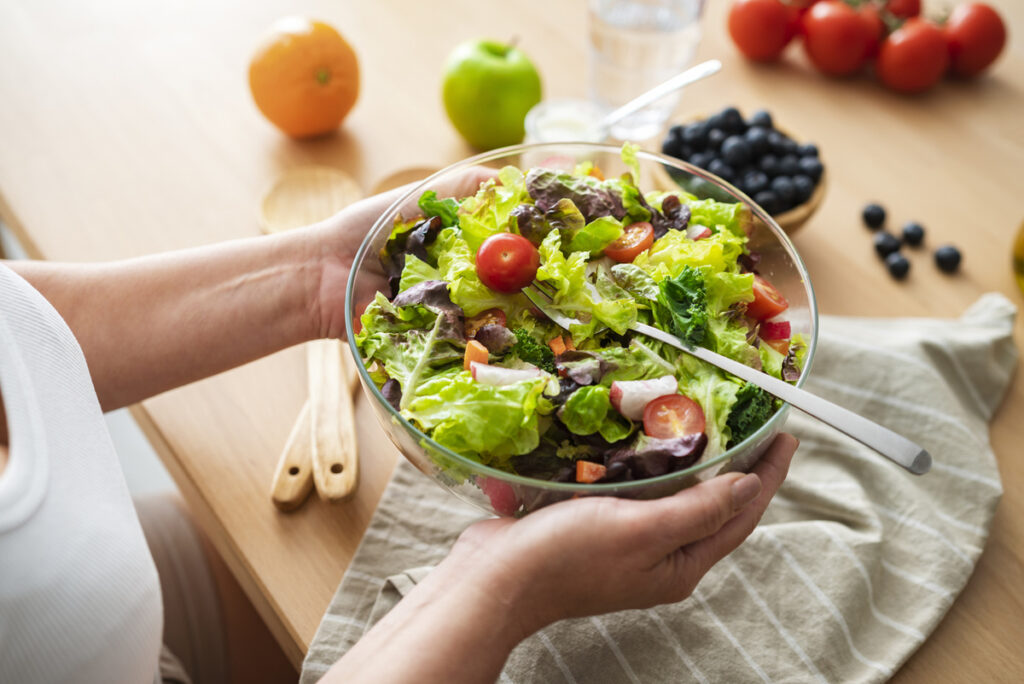 Mani di donna che reggono ciotola con insalata e pomodorini