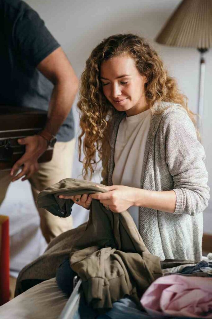 Donna con in mano vestiti e valigia vicino