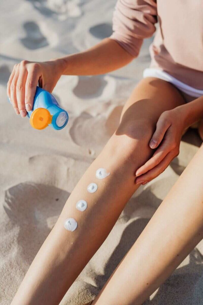 corpo di donna in costume, mani applicano crema sulle gambe