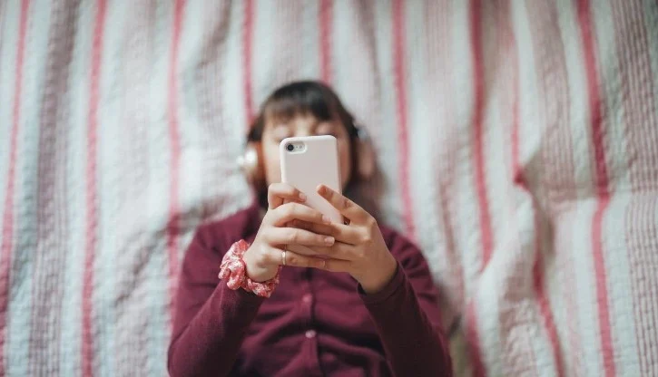 ragazzina stesa a letto guarda lo smartphone