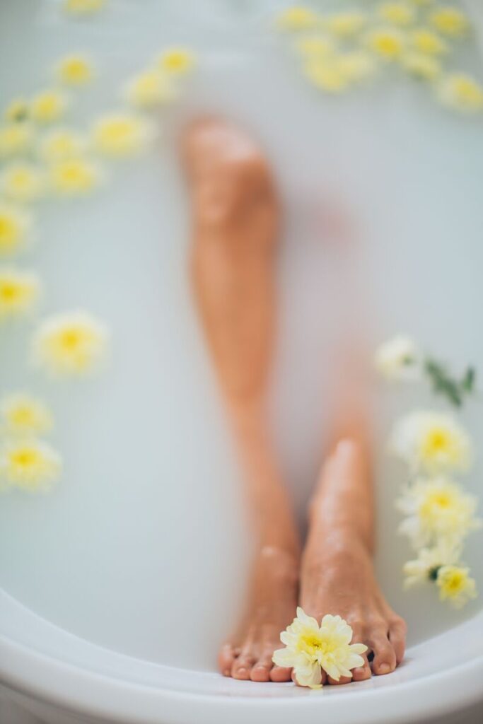 gambe e piedi di donna in vasca con acqua e fiori gialli