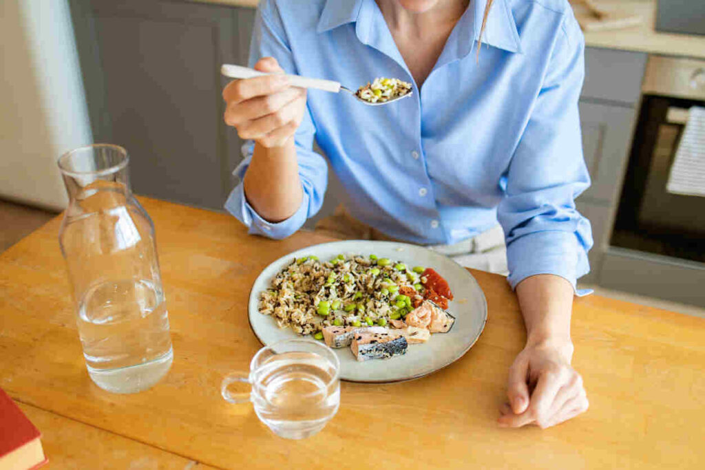 donna seduta al tavolo che mangia piatto sano con brocca d'acqua vicino
