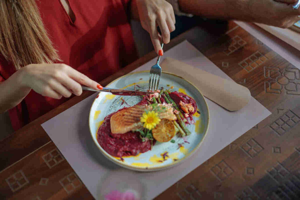 mani di donna che tagliano secondo piatto di pesce decorato con fiore 