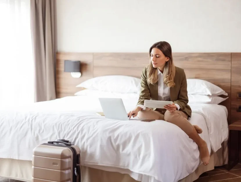 Una donna scrive al computer seduta sul letto della camera d'hotel