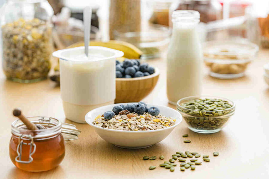 tavola con alimenti: yogurt, semi di zucca, avena e miele