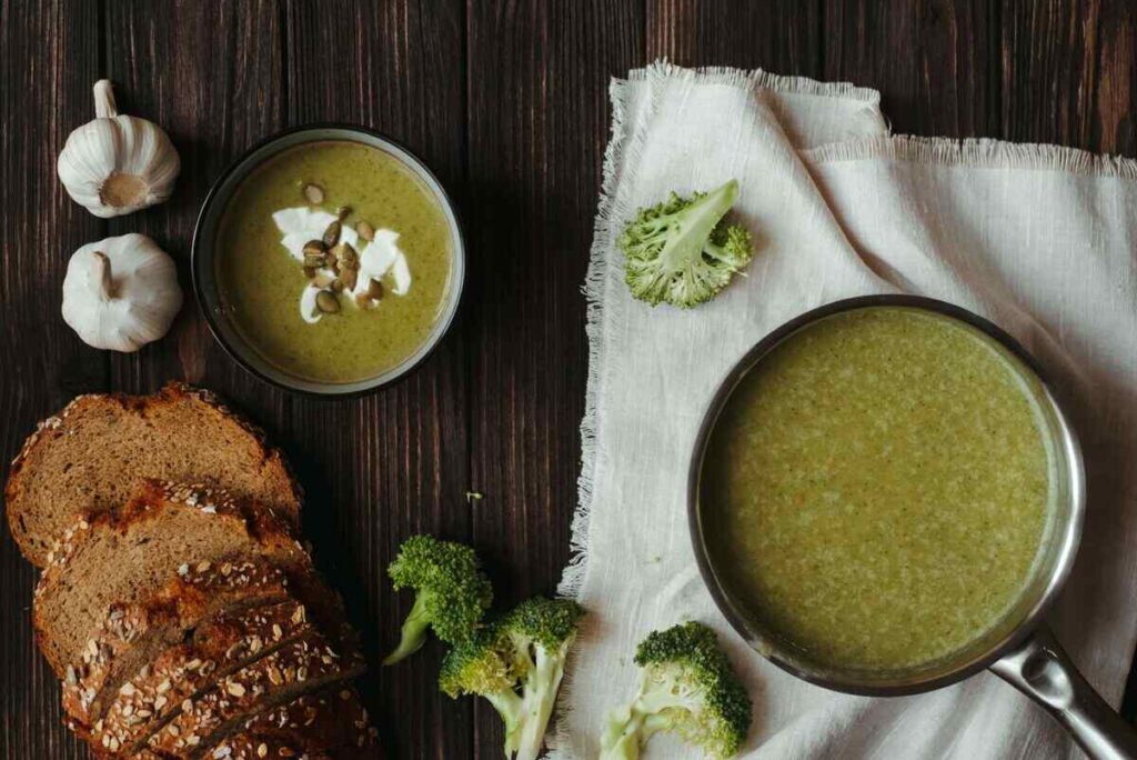 tavolo con sopra piatto con crema di broccoli, aglio e pane ai cereali