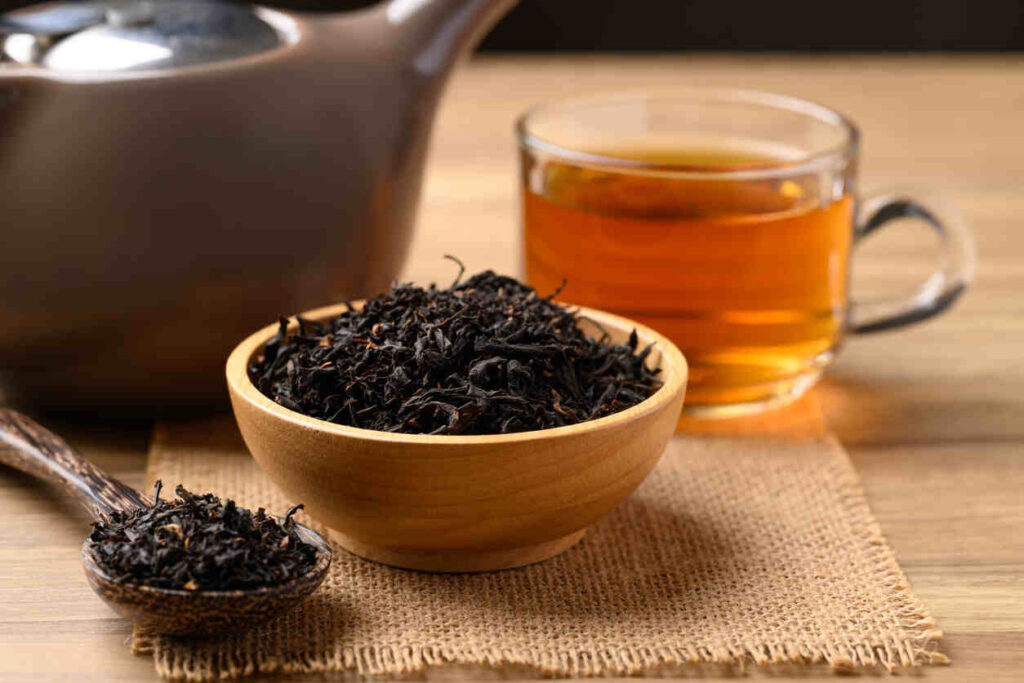 Foglie di tè nero essiccate e bevanda calda al tè in tazza di vetro
