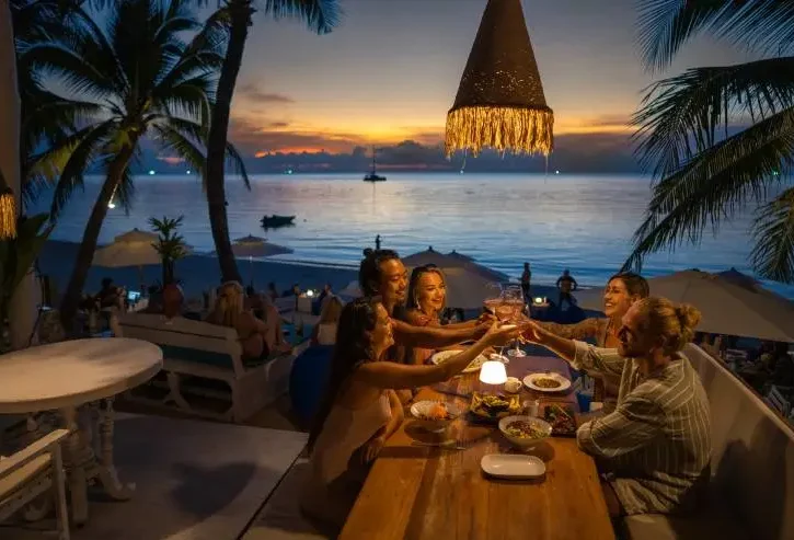 quattro amici cenano insieme al tramonto, davanti al mare
