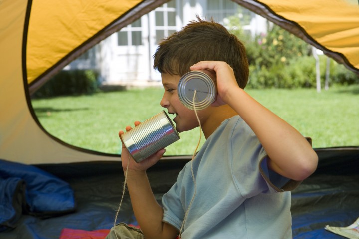 Boy (8-10) sitting on sleeping bag inside tent on garden lawn, playing with tin can phone, profile --- Image by © Juice Images/Corbis