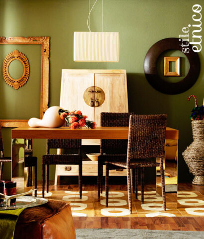 <p>Legno e accessori etnici prevalgono in questa sala da pranzo. La parete <b>verde muschio</b> valorizza e unisce i vari elementi.</p>