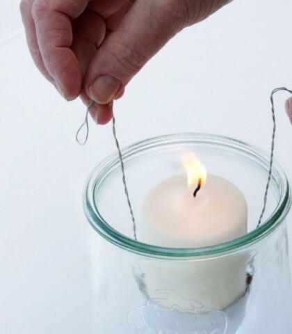 <p> <b>Così non si sposta</b><br />Inserisci la candela nel vasetto afferrando i due manici di filo di ferro. Quando la candela si sarà appoggiata sul fondo, aggancia il filo di ferro al vasetto piegandolo verso l’esterno.</p>